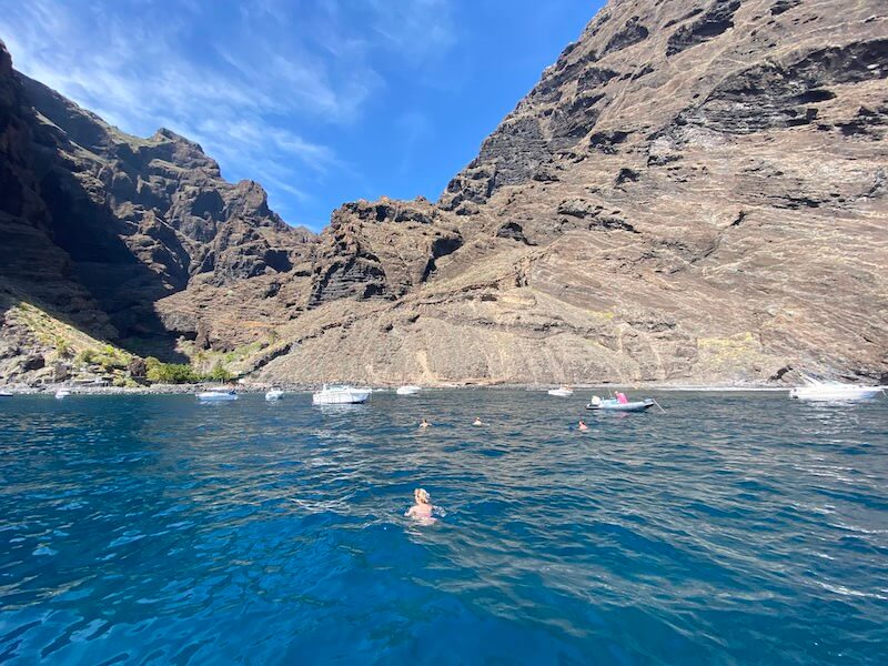 A person in the water in Tenerife in the winter with baots around the water on a sunny day