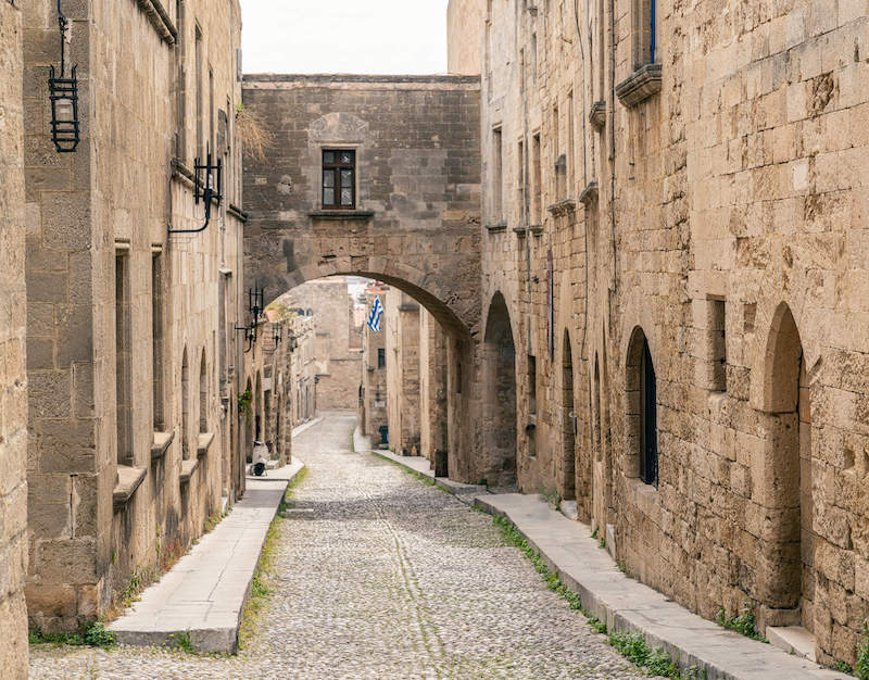 A marvelous downtown view of the Rhodes old town region with a covered archway and beautiful walkways down the cobblestone old town