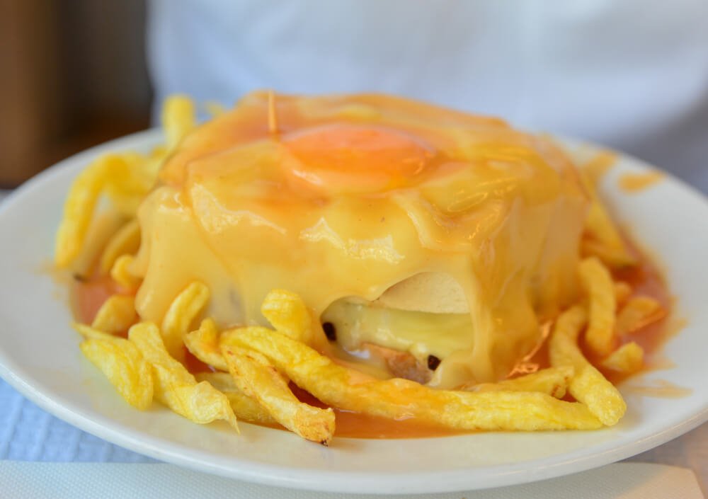 The francesinha sandwich of porto covered in cheese, a fried egg, and surrounded by fries