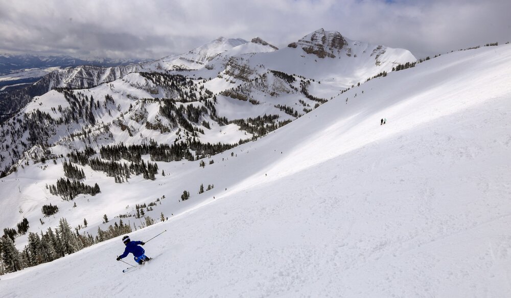 Person skiing through fresh powdery snow in Jackson Hole in winter with cloudy sky and mountain landscape covered in snow