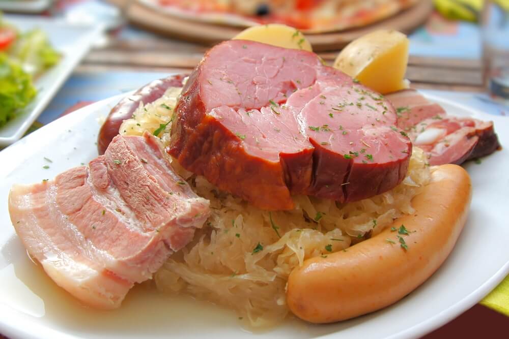 Plate of Strasbourg local food, Alsatian cuisine of assorted meats including ham, sausages, and sliced pork, served with sauerkraut and a boiled potato.