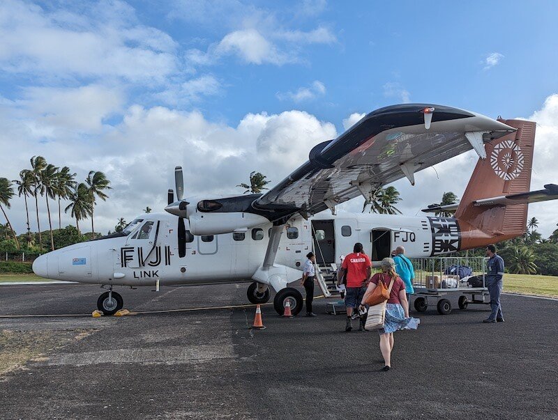 A small fiji link airplane with just a few seats on it which is what you take to taveuni. people walking out on the runway on a sunny day in fiji on a small plane