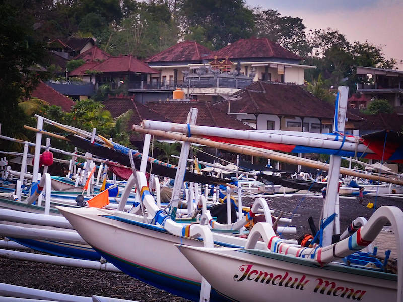 Traditional boats on a black sand beach in Amed, Bali, at sunset colors