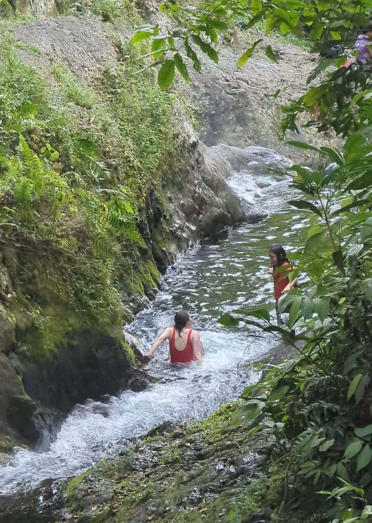 Allison on the natural water chutes in Waitavala Water Slides in Taveuni, with a little girl cheering her on as she goes down the waterfall in the lush green area