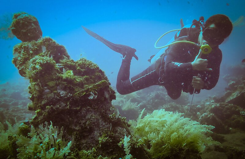 Dive instructor next to a buddha statue underwater