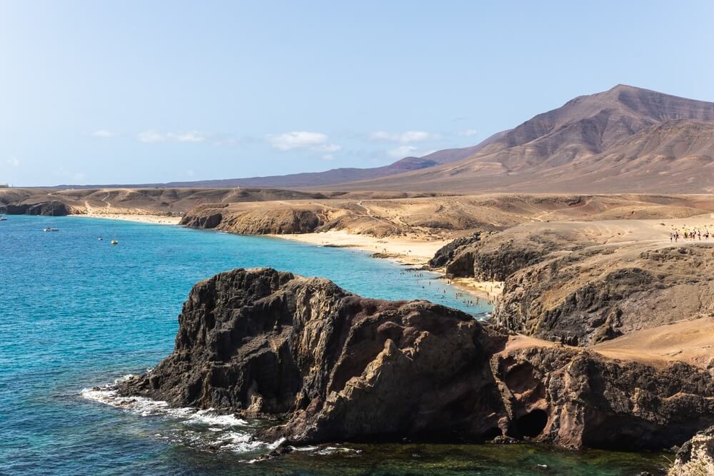 Rural landscape with multiple beaches carved out into coves of the volcanic landscape, with mountains and rugged desert-looking terrain elsewhere surrounding the beaches