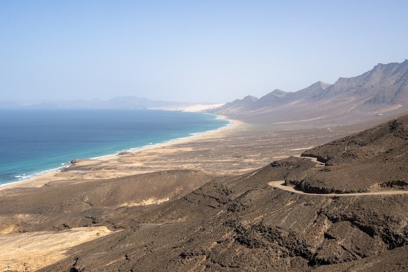 High mountains lining the west-south coast of the Atlantic ocean with turquoise water and bright blue sky, hiking in Gran Valle de Cofete