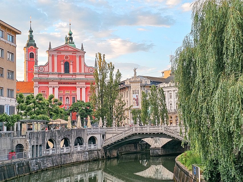 The famous triple bridge of Ljubljana with a pink church in the background on a sunny day