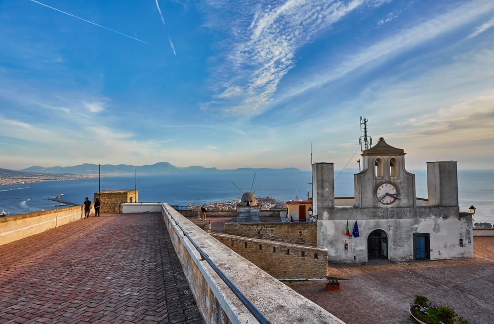 View of the clocktower of the Castel st Elmo in Vomero Hill in Naples with view of the bay, people viewing the castle in winter clothing.