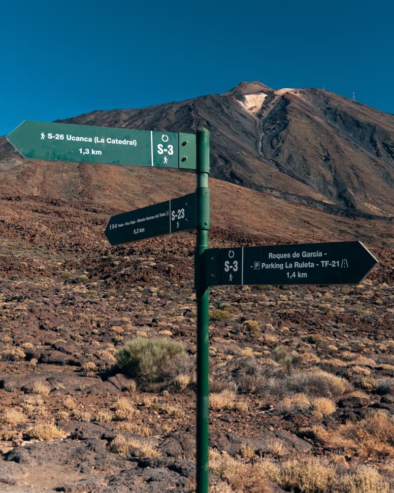 Trail signs on the Roques de García trail with a volcano in the background. Peak of the Mount Teide in the distance with the apparatus for using the cable car to get to the top