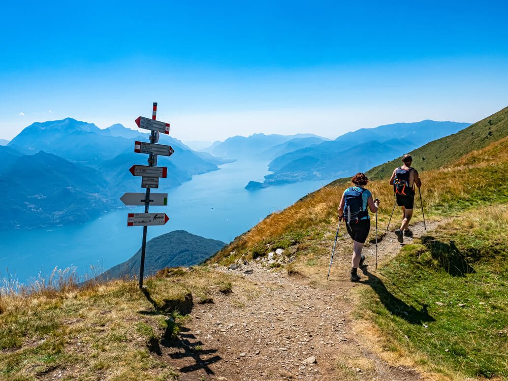 People hiking on a pathway above Lake Como in the summer wearing shorts and using hiking walking sticks