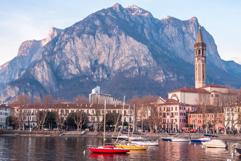 Lecco's famous clock tower and some boats on the water in the winter season with trees with bare branches (no leaves) 