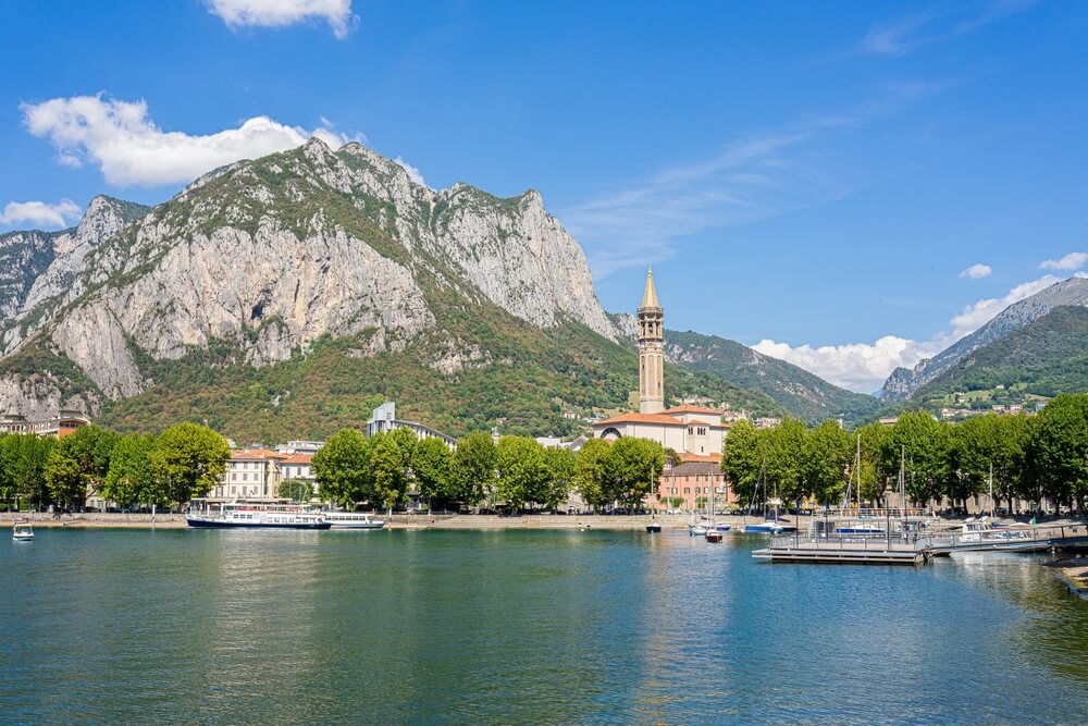 Views of the Lecco area with churches and mountains and belltowers and boats on the water 