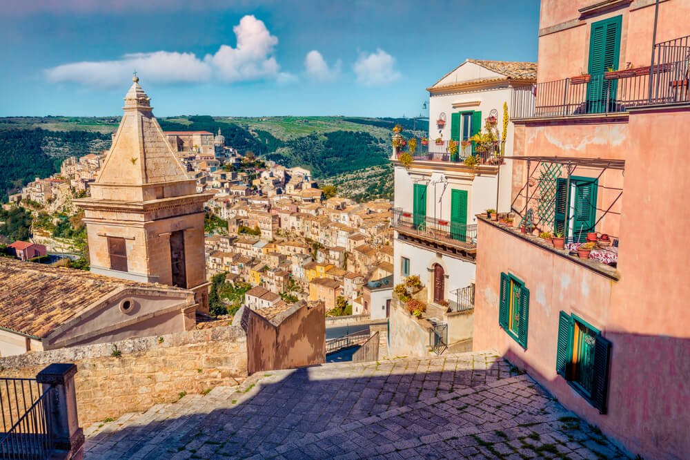 Pink pastel cityscape of Ragusa town with Church of St Mary of the Stairs and belltower and clouds in the distance
