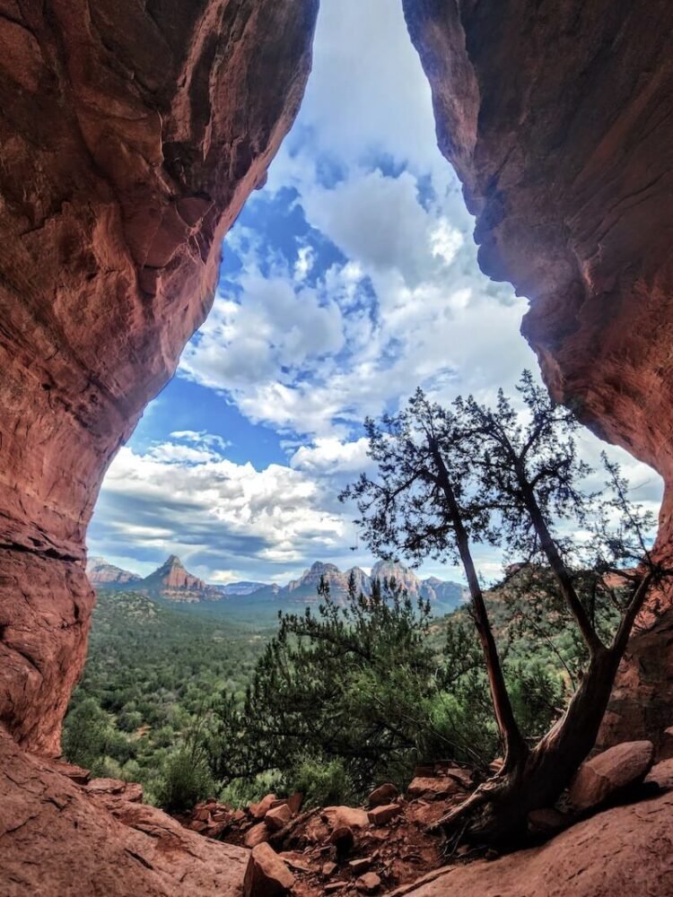 cave called the birthing cave opening to reveal red rock landscape of sedona with trees and cloudy sky