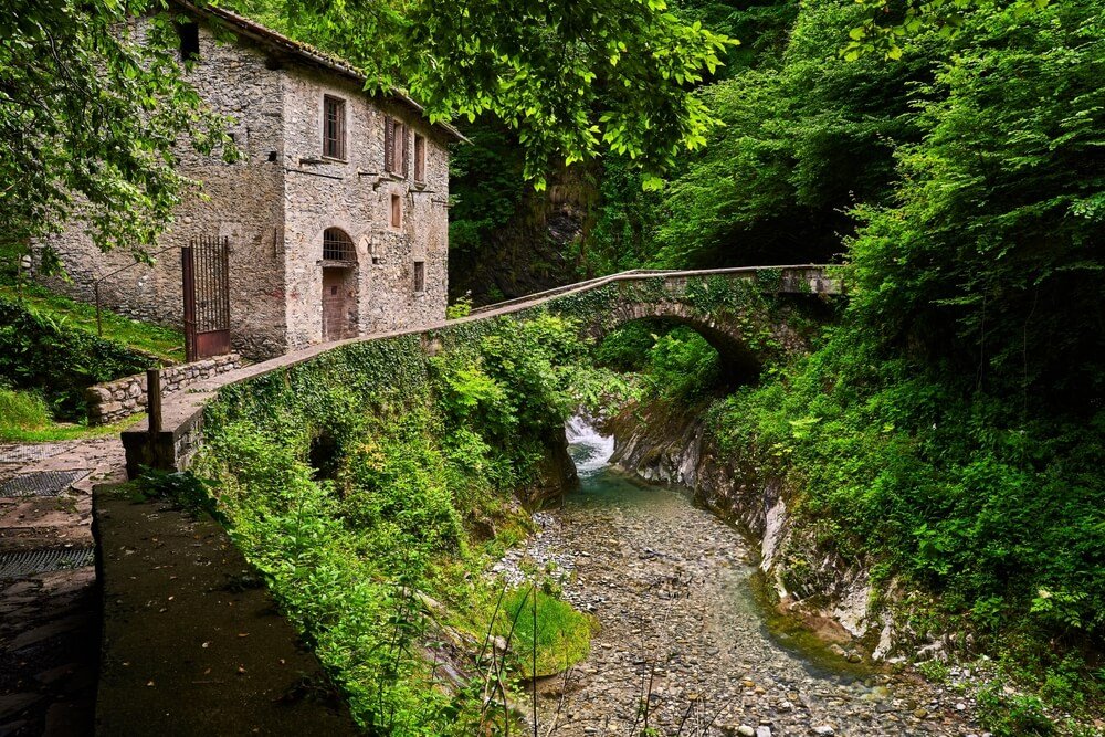 small pedestrian archway bridge and stream and stone architecture and beautiful green forest everywhere surrounding the hiking pathway
