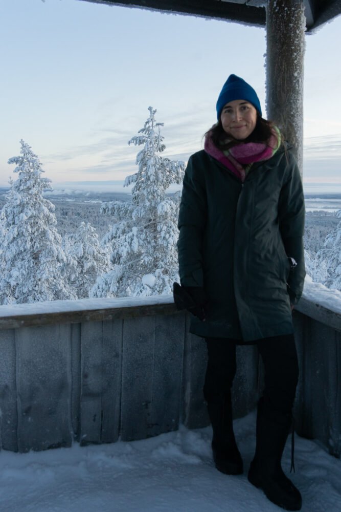 Allison Green standing in the observation tower at the top of the hill with the view of Rovaniemi behind her