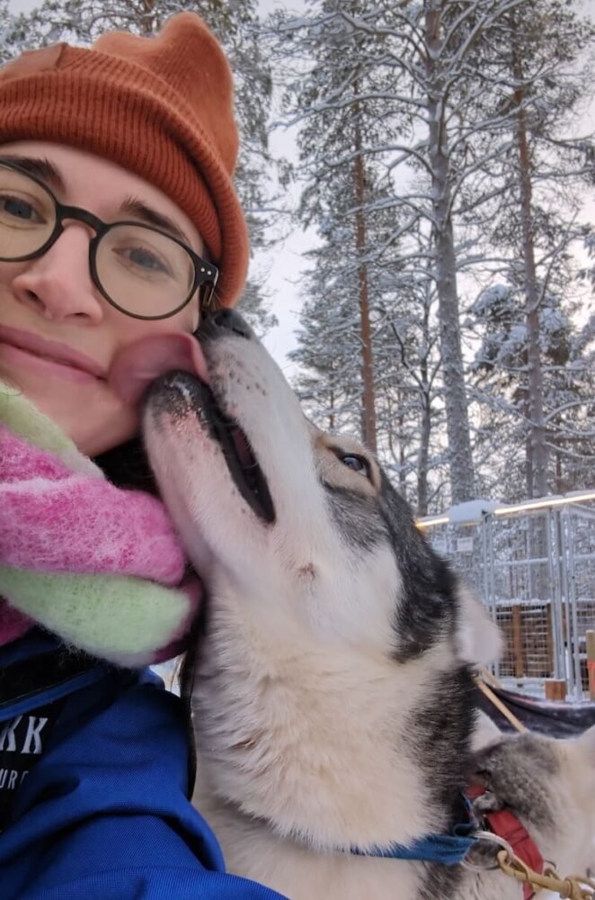 Allison Green and a sled dog giving her kisses on the face after the run