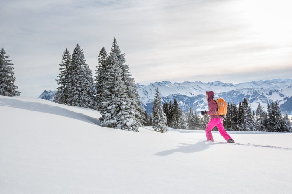 A woman in bright colors snowshoeing in the mountains of Switzerland's Alps region