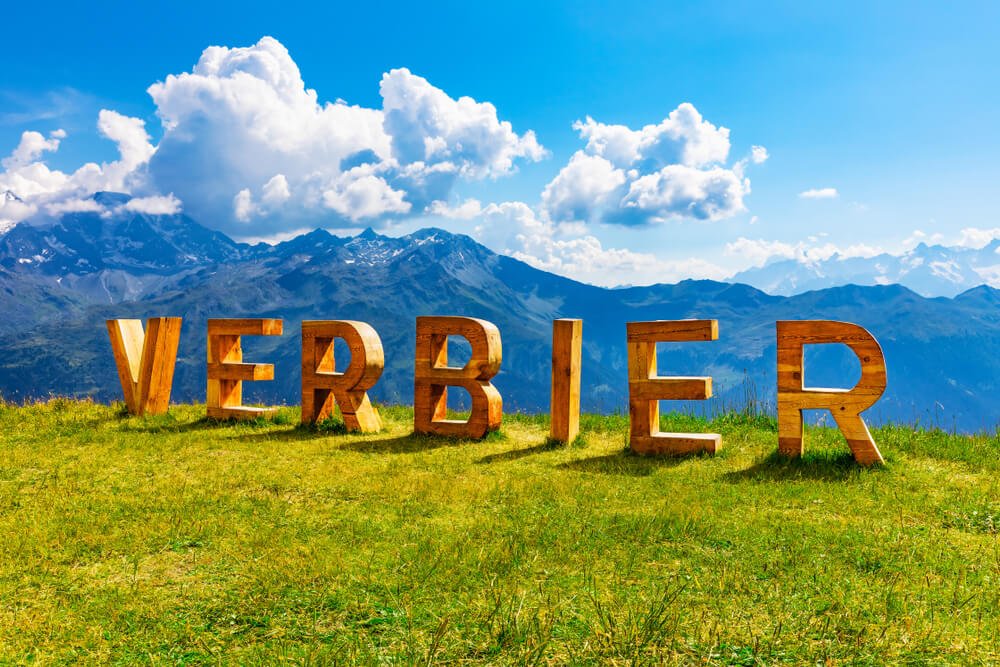A sign that says Verbier with a view of the mountains behind it