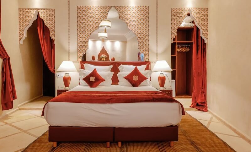 Red curtains and pillows and bed details of one of the popular rooms in this Marrakech riad