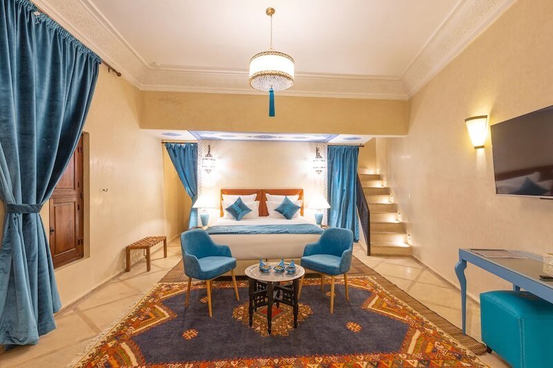 Room in a Marrakech riad with blue curtains, pillows, and details, with stairs leading down to the bedroom area