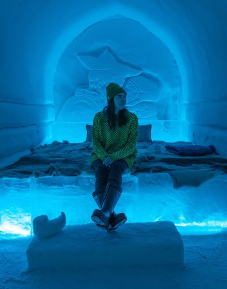 Allison Green sitting in an ice hotel in Norway with a yellow sweater and snow boots