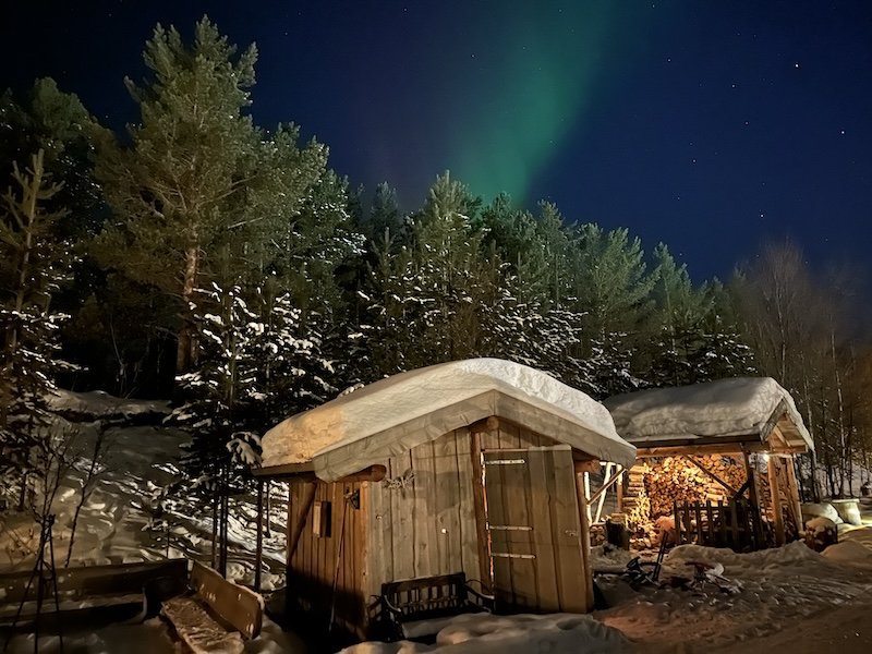 Mild northern lights display in alta with cabin and shed full of firewood