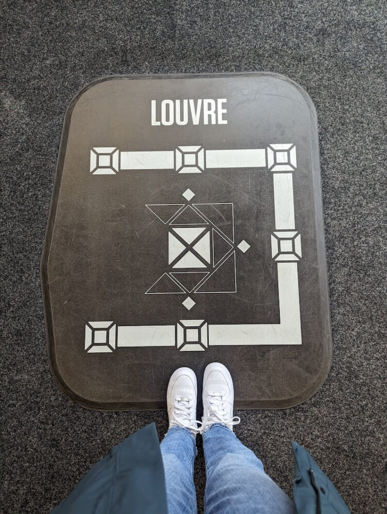 Allison standing in the Tour Montparnasse inside section looking at the Louvre, with her feet in front of it