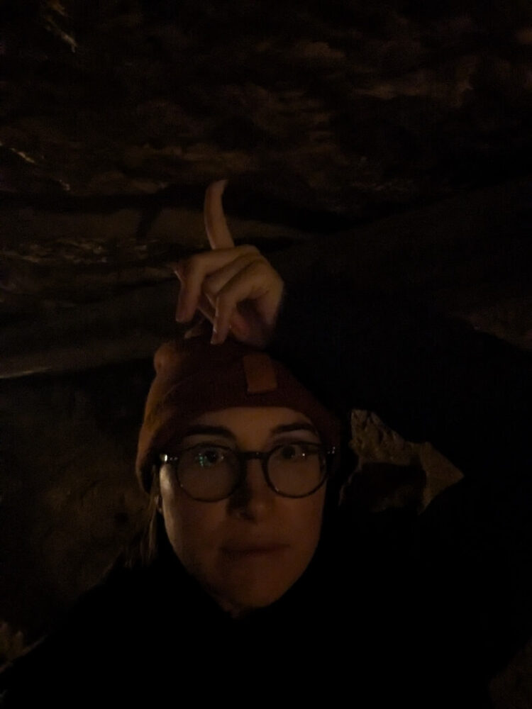 Allison Green in the dark of the paris catacombs showing just how low the ceiling is in some parts