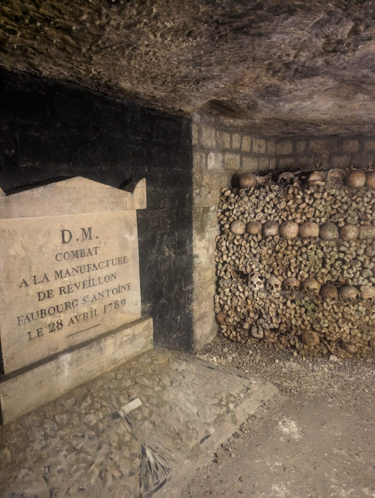 A sign that resembles a gravestone telling where the bones were from and lots of bones interred in the catacombs