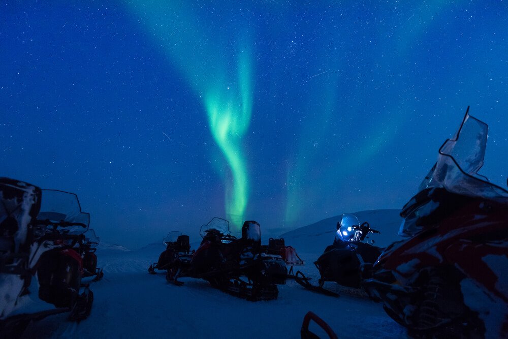 People on a snowmobile tour exploring the Northern lights wilderness in Svalbard