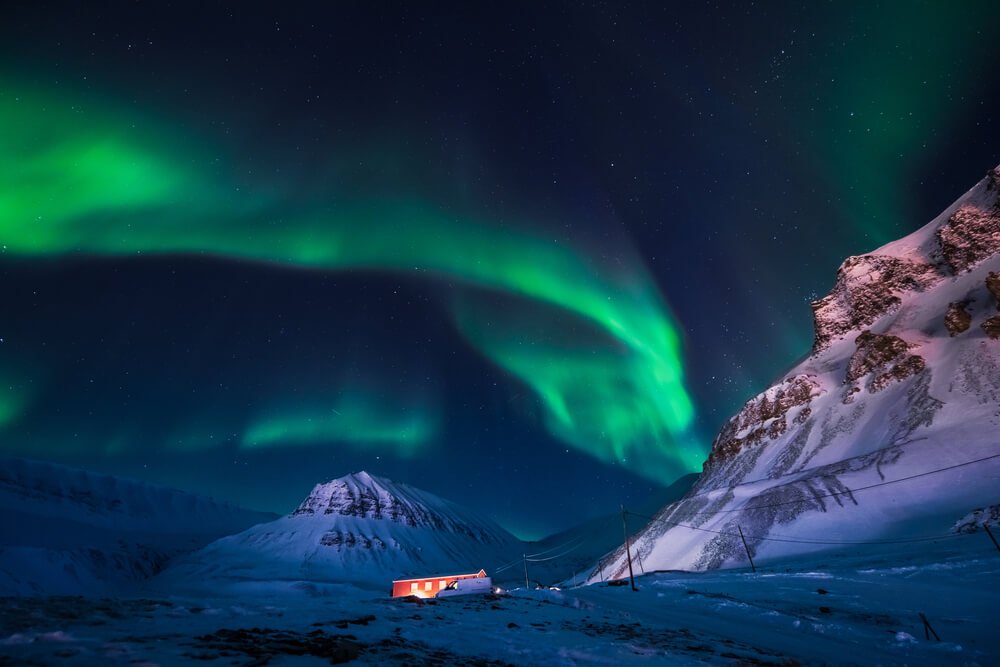 Brilliant spiral of green light emanating from the sky during winter in Svalbard showing beautiful Northern ligths display in the sky with snow covered mountain in the background