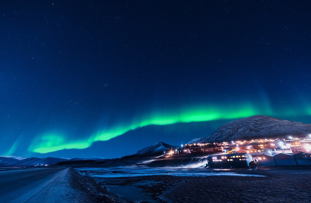 One small band of the Northern lights appearing over the town lights during the winter in Svalbard