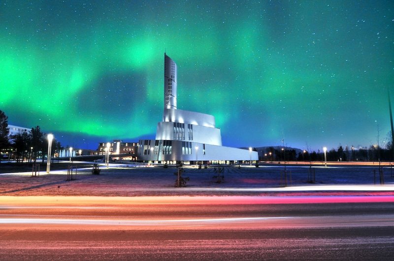 The bright dancing lights of the aurora in Alta City with the northern lights cathedral and light trails from cars in the foreground