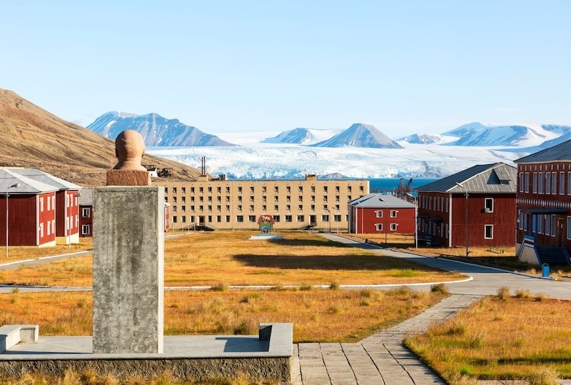 A summertime view of the  abandoned Russian arctic settlement of Pyramiden, a former mining town,  with the bust of Lenin on display and a glacier in the background