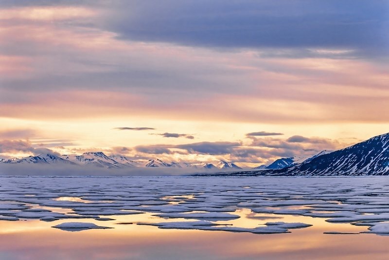 The warm light of the midnight sun being cast on ice in the fjords, a contrast between winter and summer