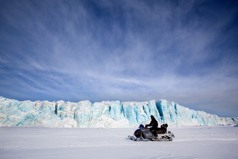 A glacier in Svalbard, Norway with a person traveling on a jet ski on a sunny day in March in sunny winter