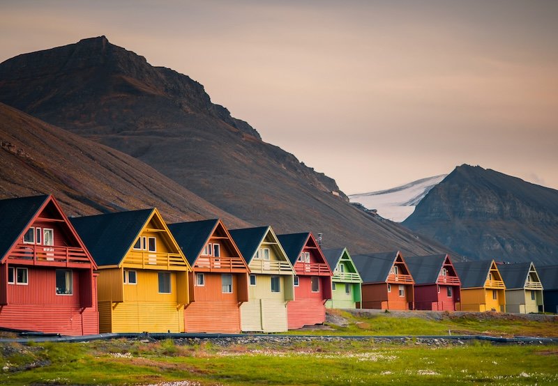 The colorful houses of Longyearbyen next to tundra landscape with some green grass and orange growth on the mountains