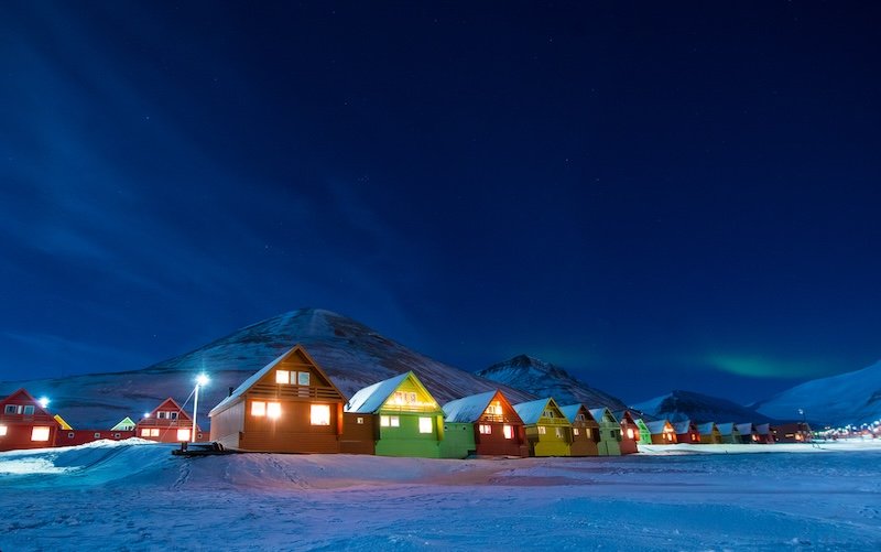 The colorful houses of Longyearbyen with a light dusting of snow and just a little hint of the aurora in the distance