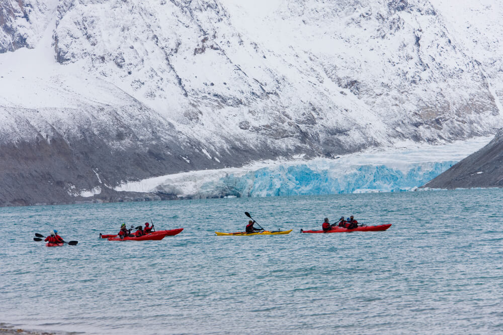 People kayaking in front of glaciers in the arctic ocean in svalbard