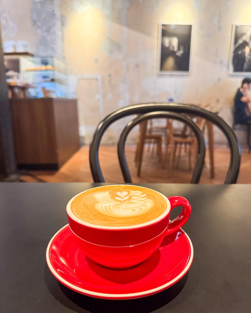 A red cup for coffee with a flat white inside and interior of the cafe visible behind me