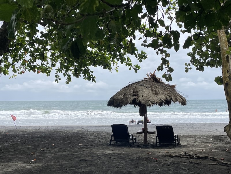 A lonely umbrella with two beach chairs on a black sand beach overlooking the beautiful water in the Caribbean coast of Costa Rica en route to Bocas del Toro