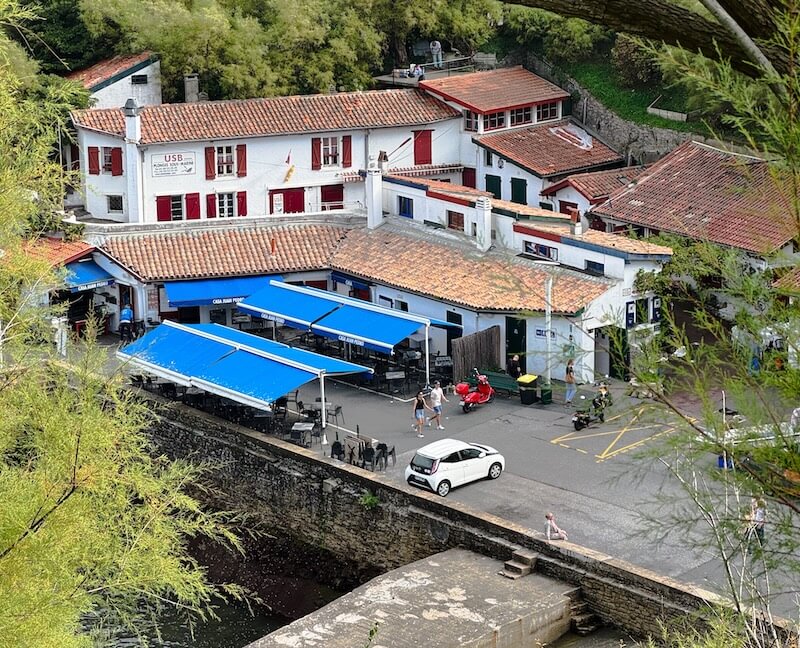 Biarritz’s Port des Pêcheurs marina with white seaside buildings, blue awnings, and people strolling along the waterfront, enjoying the lively harbor atmosphere.