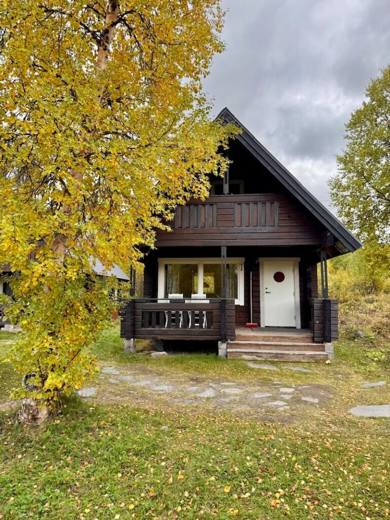 Dark wood A-frame style cabin in the autumn with yellow leaves on the tree