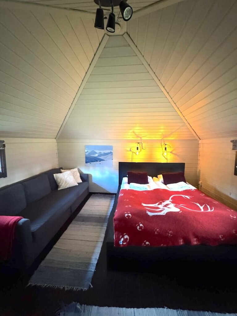 Interior of the reindeer lodge chalet with high ceilings, bed, sofa, and light details with antlers