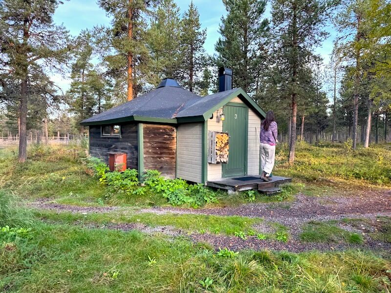 Stohpu forest cabin exterior with Allison standing on the porch in the forest
