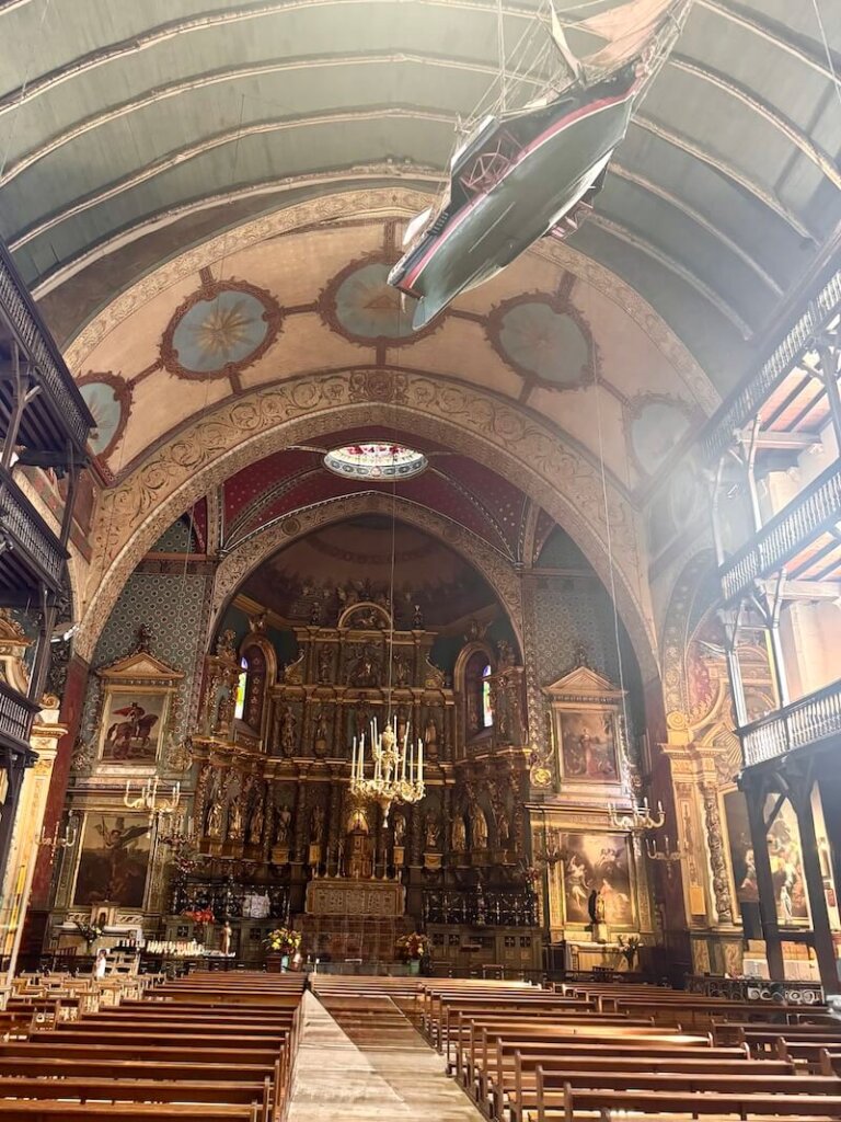 The interior of the main church in St Jean de Luz, with a model ship hanging from the ceiling, and an altar and pews