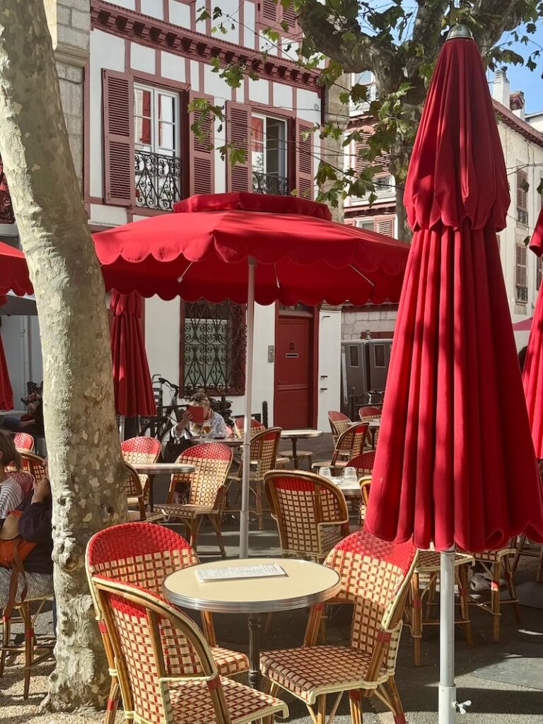 An outdoor seating area with typical bistro style chairs and umbrellas in the main square of St Jean de Luz