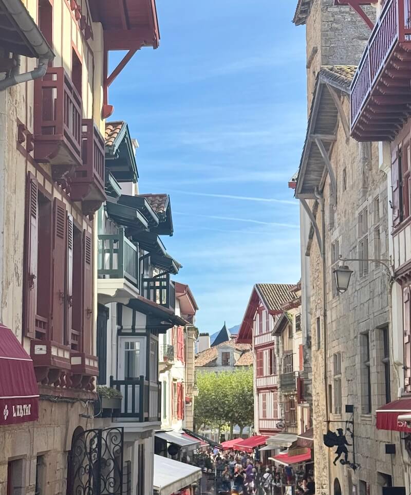 View of one of the streets leading to the main square in Saint jean de luz with typical basque country architecture and lots of people in the streets enjoying the weather